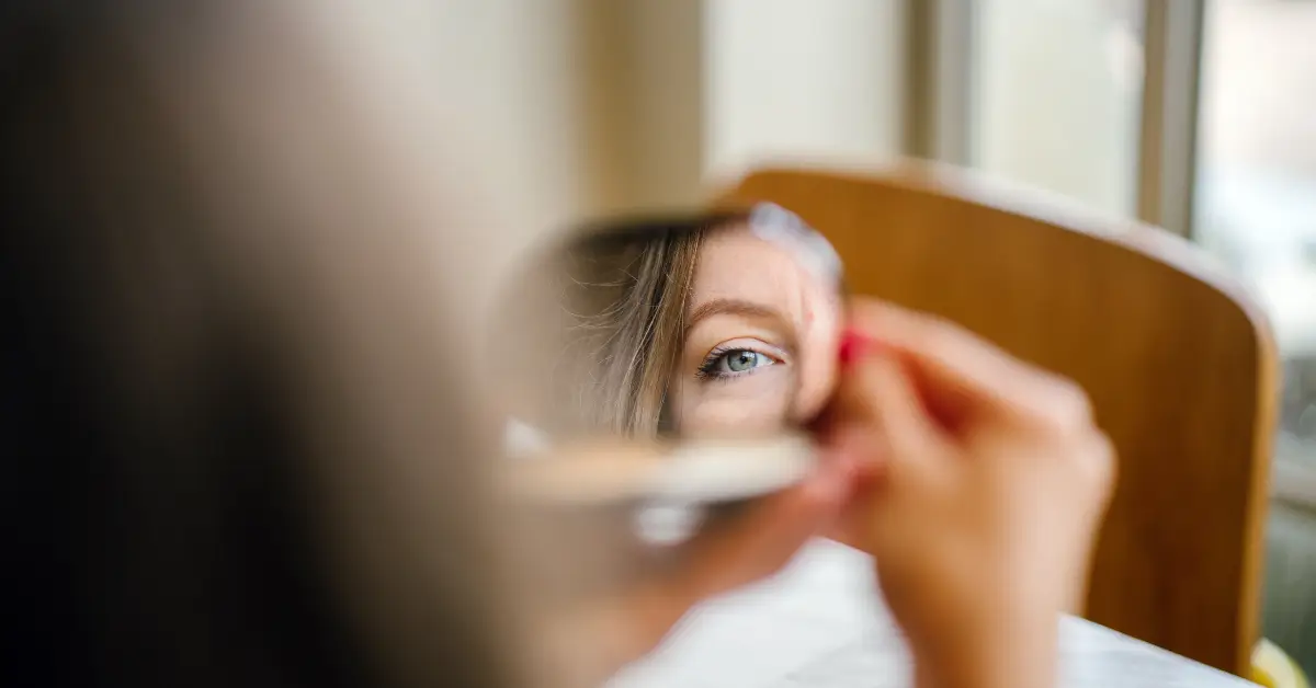 Who You Are: A woman (midlife, natural light, minimal makeup) looking into a mirror—not with vanity, but with softness or even uncertainty.